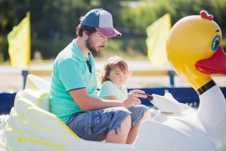 Little girl and her father at amusement park on the boat, family activity