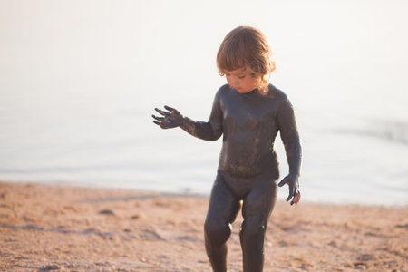 Toddler kid covered with black health mud, water on the background, having fun, copyspaceの写真素材