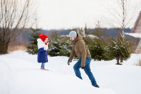 father and his toddler daughter walking together at snowy park, playing snowballs, having fun, winter activityの写真素材