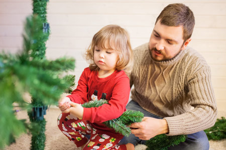 Father and daughter assembling christmas tree, smiling - christmas, holiday, winter concept, family activityの写真素材