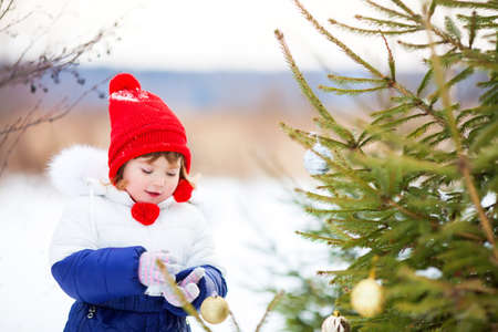 Cute little girl decorating Christmas three outdoors, winter snowy dayの写真素材