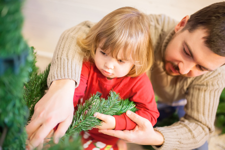 Father and daughter assembling christmas tree, smiling - christmas, holiday, winter concept, family activityの写真素材