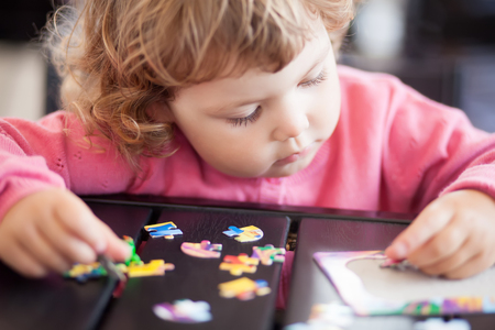 Blonde toddler girl, solving puzzle on a table, having fun. Early education and developement. Little genius concept.の写真素材