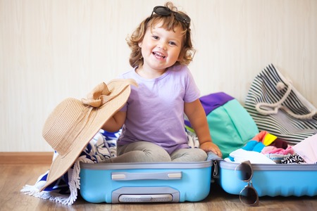 Adorable toddler girl tourist packs clothes into a large suitcase for travel, vacation concept.の写真素材