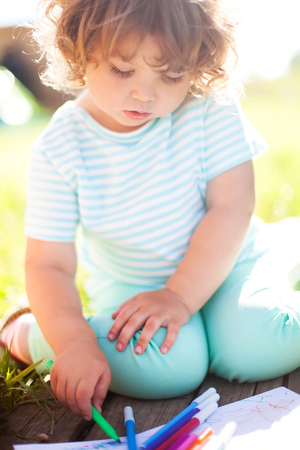 Adorable little girl drawing with felt-tip pens outdoors. Summer leisure. Talented kids, early art education.の写真素材