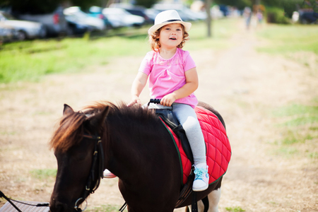 Cute toddler girl riding a horse, equestrian sport for kids, little horseman.の写真素材