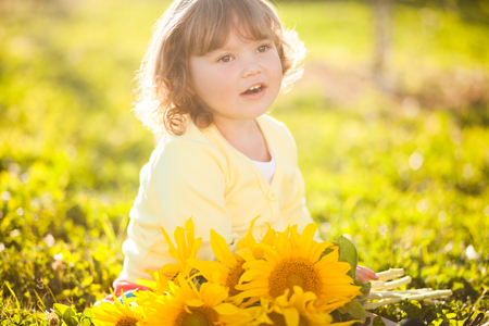 Sunny day, summer vacation. cute little girl with yellow sunflowers, outdoor portrait.の写真素材