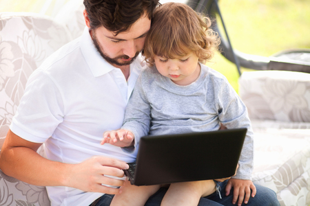 Little girl sitting on fathers knees looks at the laptop with serious pensive face. Child working with device. Early education. Wunderkind concept. Smart kid and technology. Caring loving father. Copyspace.の写真素材