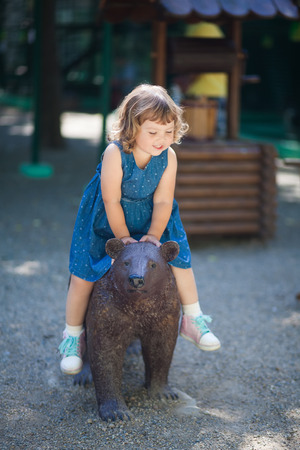 Adorable little girl in the zoo, sitting on the bear statueの写真素材