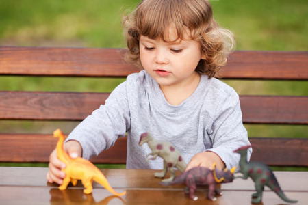 little girl having fun playing with plastic dinosaurs outdoorsの写真素材