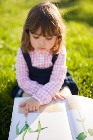 Moscow, Russia. 9 May, 2018. Adorable little girl reading botany book, learning nature in the garden. Early development education concept.の写真素材