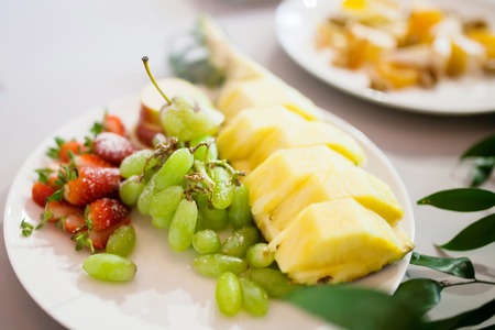 Beautiful decorated various fruits on plate at restaurant, wedding catering. Pineapple, strawberry, green grape.の写真素材