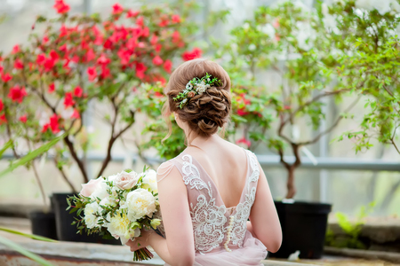 Bride in the greenhouse with tropical blooming plants, beautiful hairstyle and stylish hair accessory, holding wedding bouquet. close up, copy spaceの写真素材