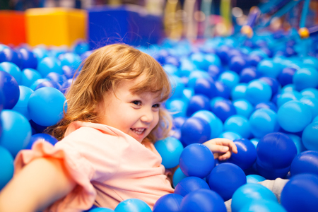 Happy little kid playing at colorful plastic balls playground high view. Adorable girl having fun indoors, kindergartenの写真素材