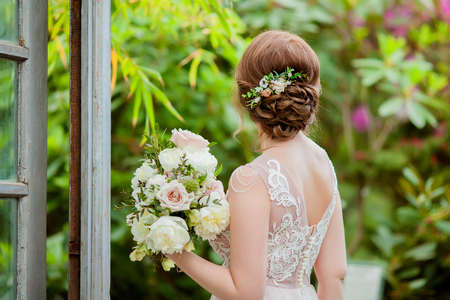 Bride in the greenhouse with tropical blooming plants, beautiful hairstyle and stylish hair accessory, holding wedding bouquet. close up, copy spaceの写真素材