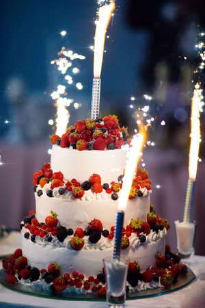 Beautiful white wedding layer cake decorated with berries - strawberry and blueberry, served with fireworksの写真素材