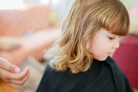 Cute little blonde curly girl at the beauty salon, children hair cut. The hairdresser doing hair style.の写真素材