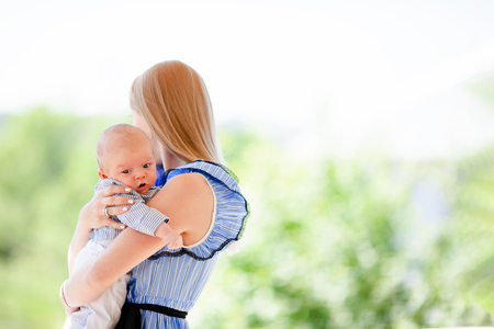 Happy mother standing at the balcony of her country house, holding a baby in her arms, family portrait of mum and childの写真素材