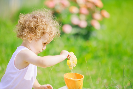Cute curly little boy playing in the sandbox outdoors, warm summer dayの写真素材
