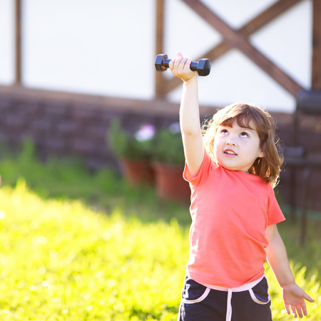 Happy little girl and her father lifting dumbbells putdoors. Active healthy life for family. Fitness. Sport for little childrenの写真素材
