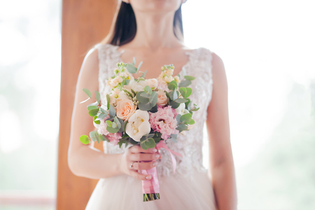 Bride holding wedding bouquet of white peony and pink roses. Lots of greenery.の写真素材