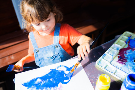 Adorable little kid girl holding paint brushes, painting picrure at the paper. Artistic preschooler, art for childrenの写真素材