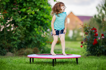 Adorable little girl jumping on a trampoline outdoors at summer day. Acivity for kids. Jealthy lifestyle.の写真素材