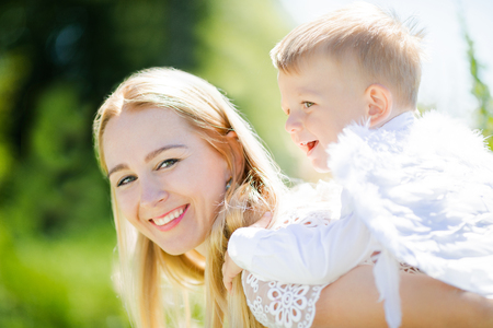 Beautiful mother and her toddler son wearing angel costumes having fun outdoors. Cheerful moment, loving family. Mom is the Guardian angel for her child concept.の写真素材