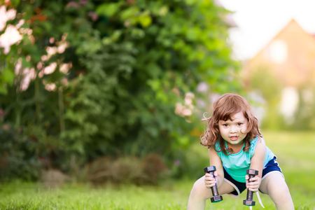 Happy little girl lifting dumbbells in the park. active healthy life. Fitness. Sport for little children.の写真素材