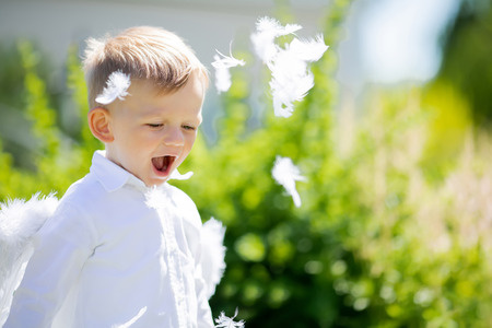 Adorable toddler boy in angel costume playing with white feathers outdoors, angelic child. Saint Valentines day.の写真素材