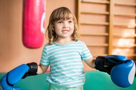 Funny smiling little boxer girl wearing blue boxing gloves, training at the gym.の写真素材
