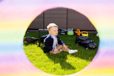Cute blond toddler boy playing with cars and other toys at his birthday party. Sunny summer day.