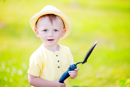 Cute toddler boy wearing straw hat standing in the garden holding little shovel, ready to work.の写真素材