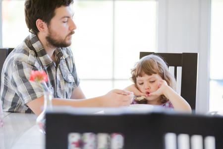 Father feeds his daughter and she doesn't want to eat. Kid refusing food. Sad childの写真素材