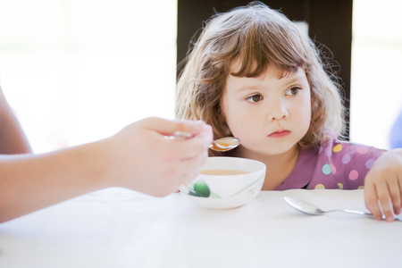 Father feeds his daughter and she doesn't want to eat. Kid refusing food. Sad childの写真素材