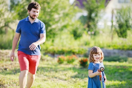 Father and daughter having fun in the garden, watering plantsの写真素材