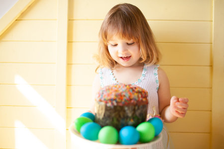 Cute girl with hand painted Easter eggs and Easter cake with yellow wooden