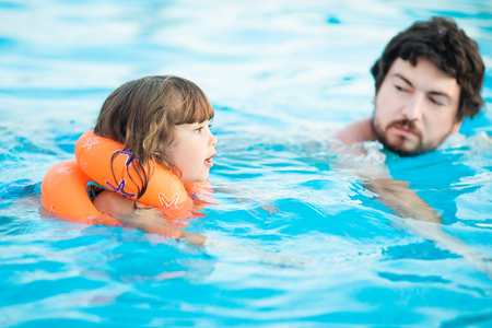 Happy family, active father with toddler daughter, having fun together in outdoors swimming pool in water park.の写真素材