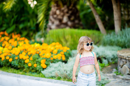 Adorable little girl wearing sunglasses, walking at the tropical resort, standing by the palm three...