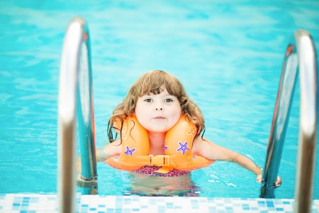Adorable little girl with inflatable life vest having fun, learning to swim in the pool.の写真素材