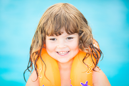 Adorable little girl with inflatable life vest having fun, learning to swim in the pool.の写真素材