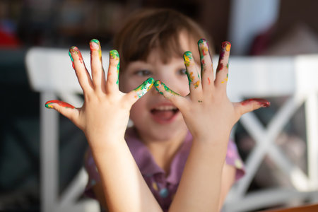 Cute little preschool gir having fun, looking at her painted hands and smiling. Education, school,...