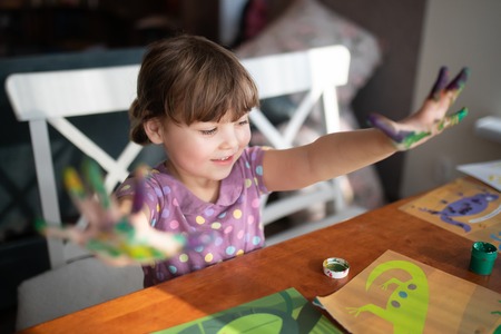 Cute little preschool gir having fun, showing her painted hands. Education, school, art and painitng conceptの写真素材