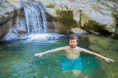 Young man enjoying swimming in a waterfall in a forest aloneの写真素材
