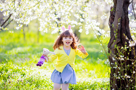 Adorable little girl playing in blooming  tree garden on Easter egg hunt, running and smiling.の写真素材