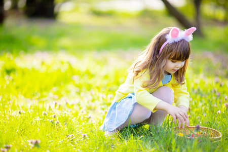 Adorable little girl playing in the garden on Easter egg hunt, searching eggs in the grass at spring...