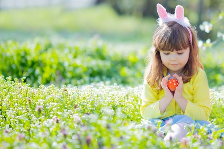 Cute little girl with curly hair wearing bunny ears and summer dress having fun during Easter egg huntの写真素材