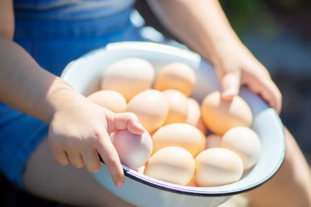 Closeup of child's hands holding basket full of white and brown raw eggs from farmの写真素材