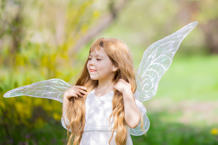 Portrait of cute little curly blonde Angel Fairy girl smiles and teases. Spring day. Concept of angelic child with a bad temper.の写真素材