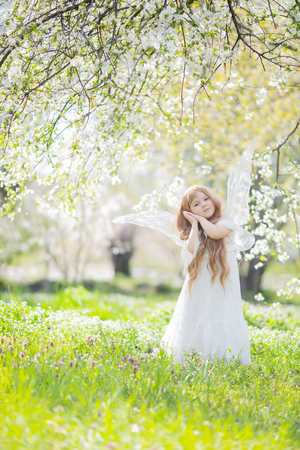 Fairy tale concept. Little toddler girl wearing beautiful princess dress with fairy wings in the forest or park, spring day, white blooming trees.の写真素材